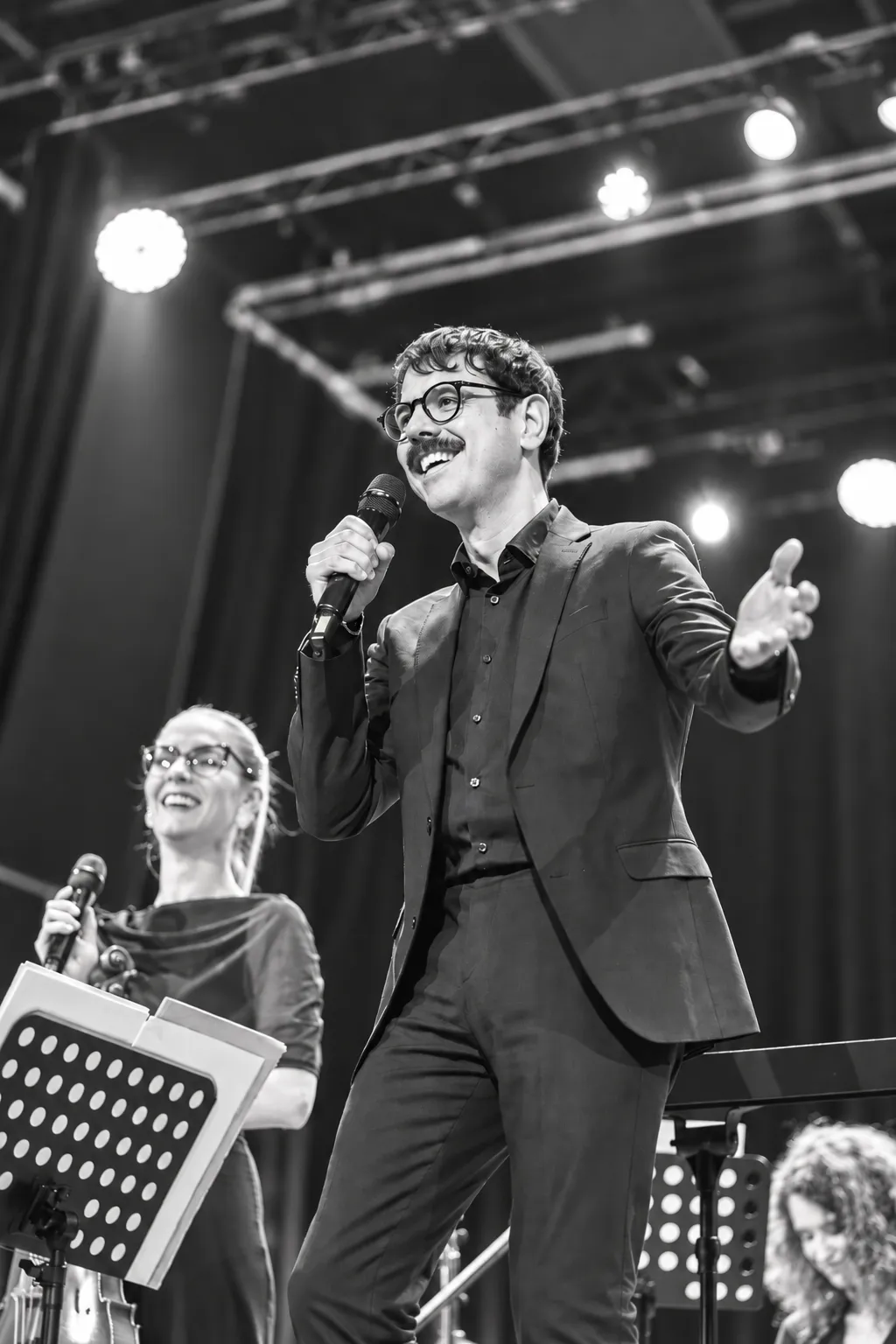 Federico Bresciani speaking into a microphone on stage, arm outstretched, during a concert